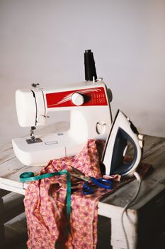 木桌上缝纫装置的特写，装有机器、熨斗、织物和工具