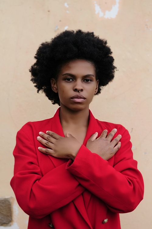 Free Portrait of a woman with afro hair crossing arms in a red coat indoors. Stock Photo