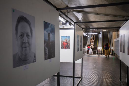 Art exhibition display in a subway with people using escalators.