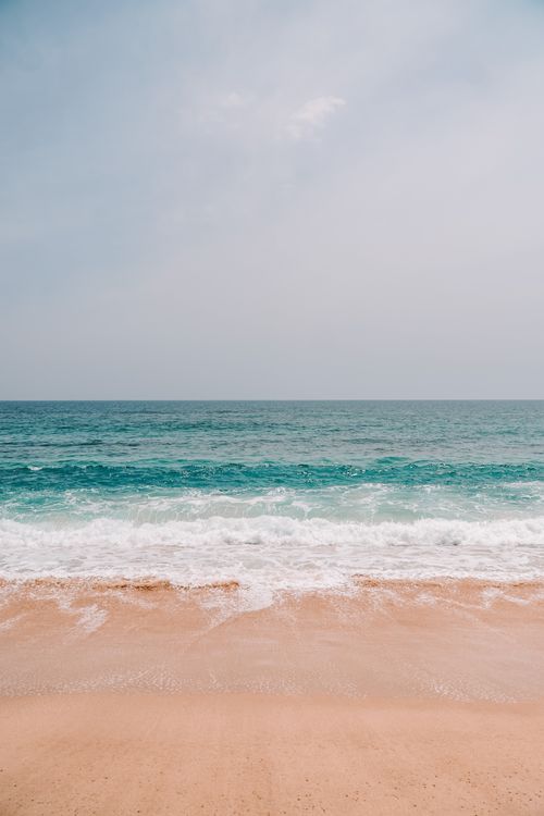 Free A serene view of waves crashing on a sandy beach under clear skies. Stock Photo