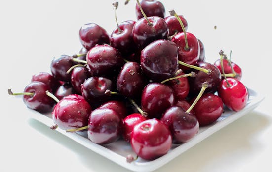 A pile of ripe, juicy red cherries on a white plate, showcasing their freshness.