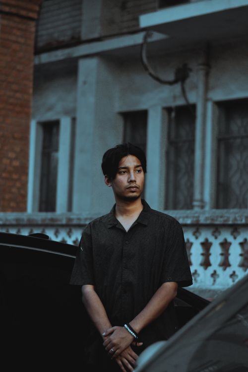 Free Portrait of a young South Asian man standing outdoors with an urban backdrop, captured in a moody setting. Stock Photo