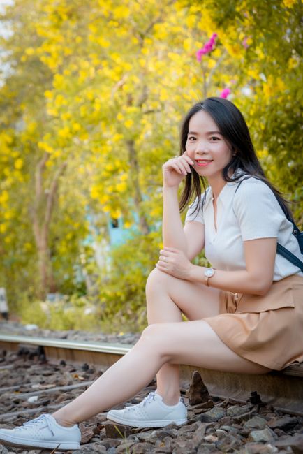 A young woman sitting by a railway in Ho Chi Minh City, surrounded by bright foliage.