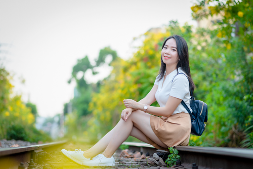 Free A fashionable young woman sits smiling on railway tracks in a sunny outdoor setting. Stock Photo