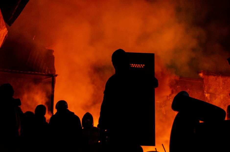 Silhouettes of protesters and smoke against fiery night backdrop in Lviv.