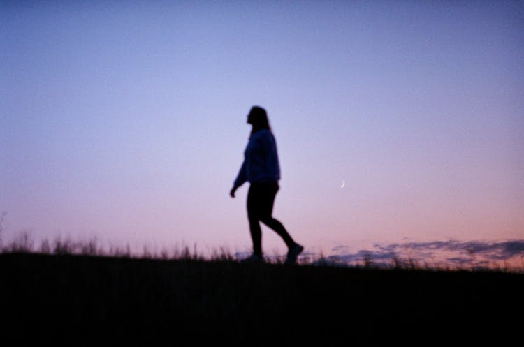 Silhouette Of A Person Walking On A Grassy Field