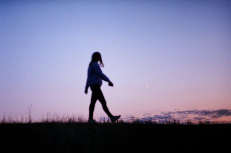 Silhouette Of A Person Walking On A Grassy Field