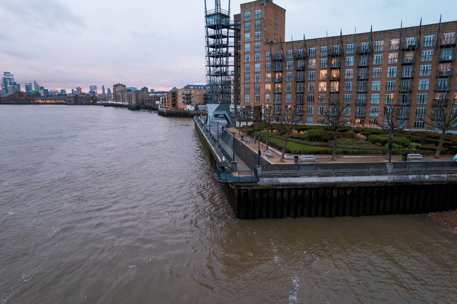 A calm evening view of riverside apartments along the Thames in London with cityscape backdrop.