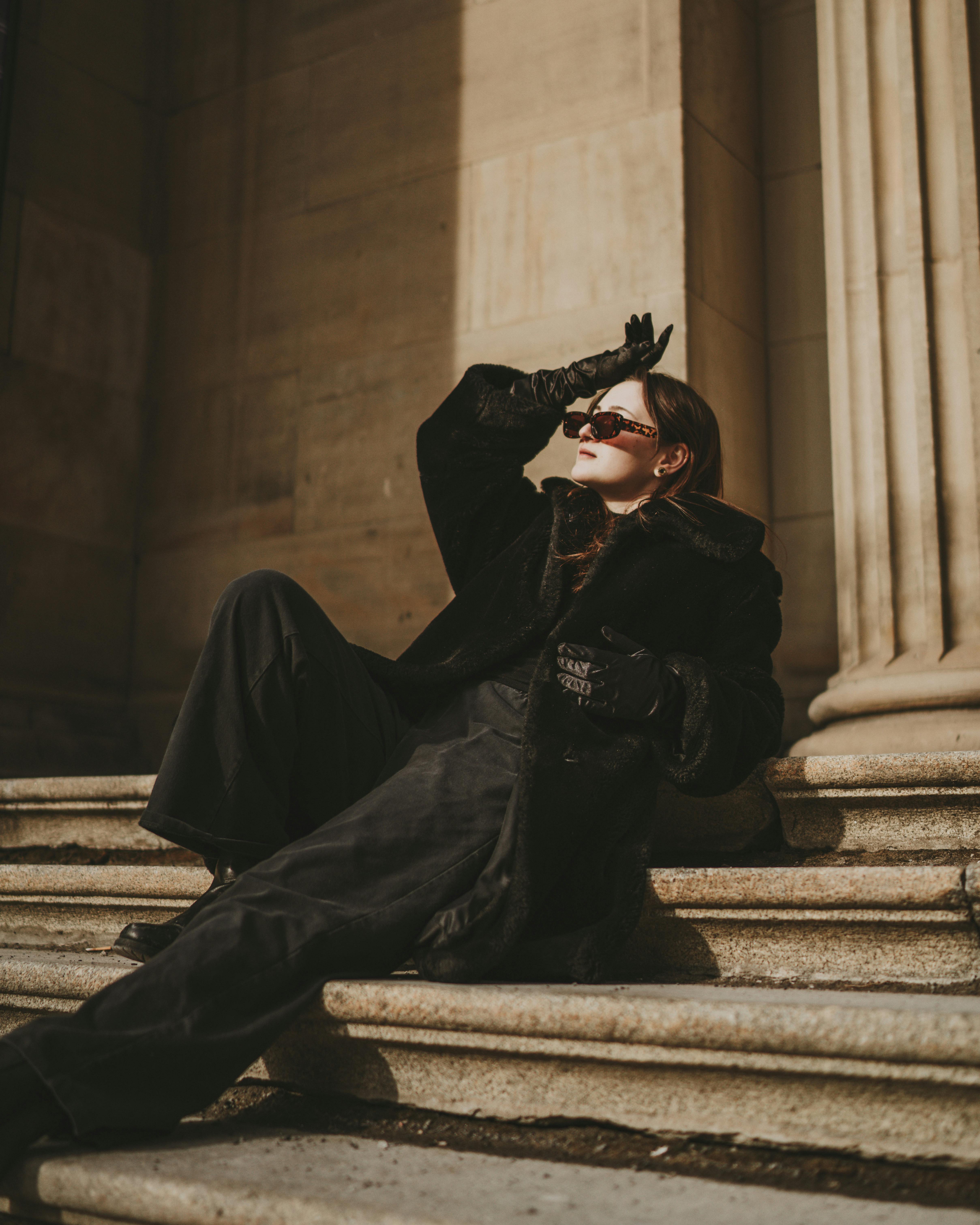 female fashion model in black warm clothes laying on stone stairs