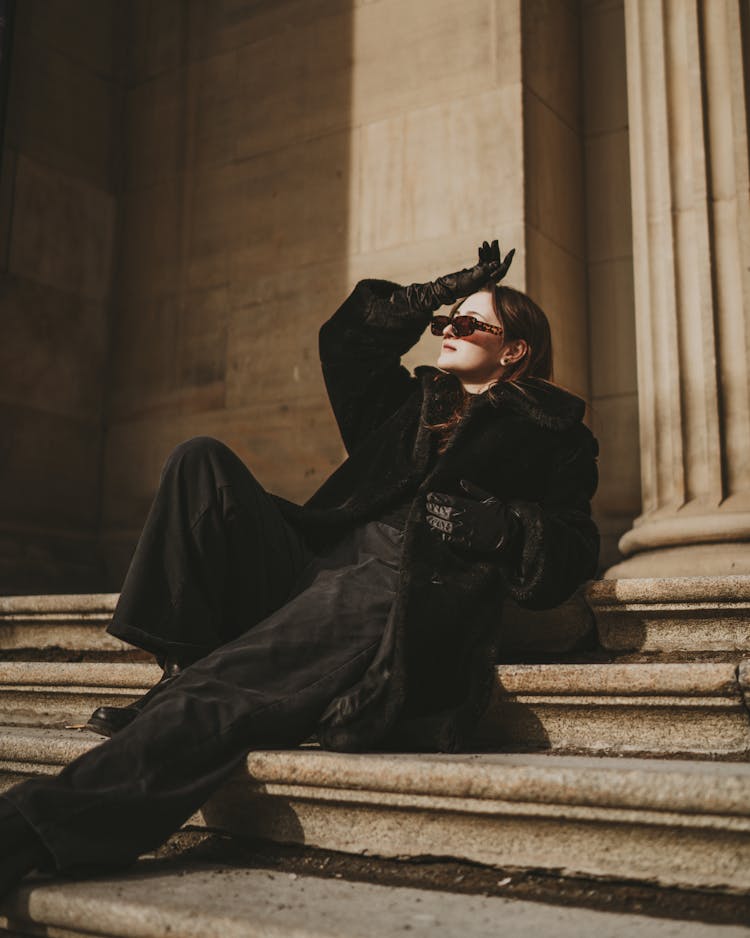 Female Fashion Model In Black Warm Clothes Laying On Stone Stairs