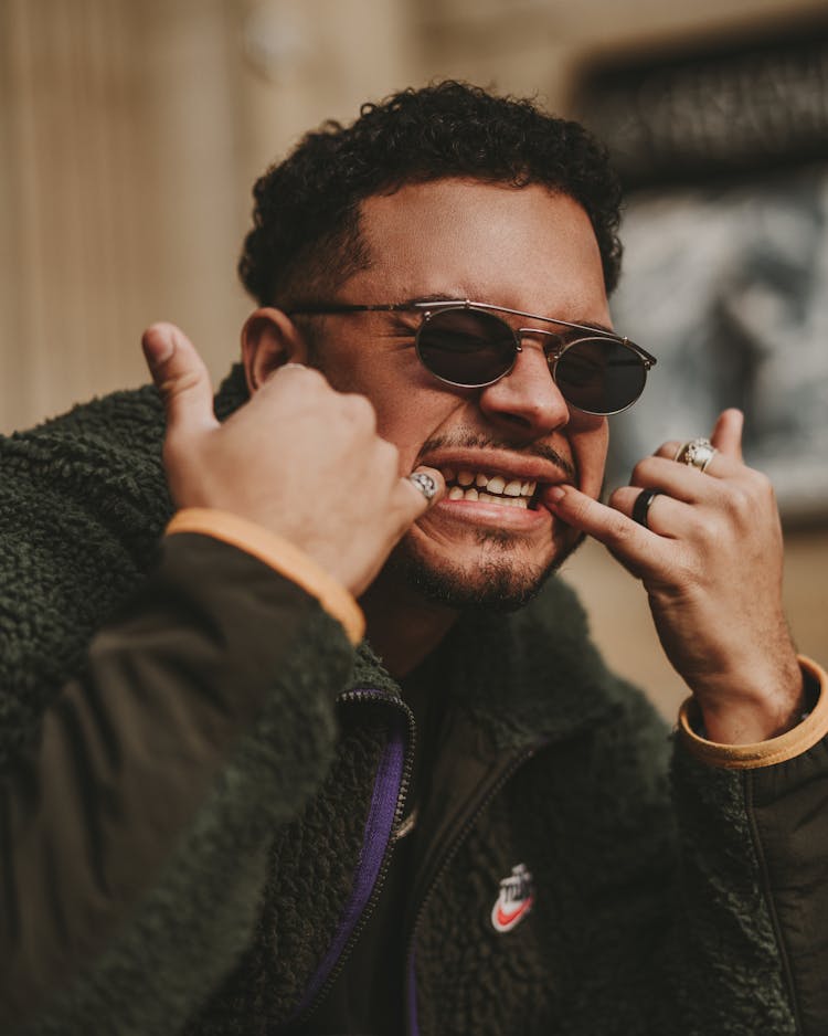 A Man In A Black Jacket Wearing Black Sunglasses And Showing His Teeth 