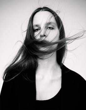 Grayscale portrait of a woman with hair blown by the wind, captured in an artistic setting.