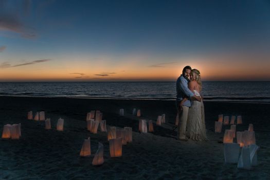 A Couple Hugging at the Seashore Surrounded by Lanterns on the Sand