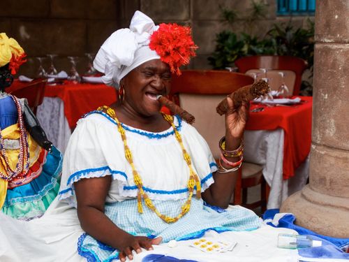 Free African woman in vibrant traditional clothing enjoying a cigar, exuding joy and culture. Stock Photo