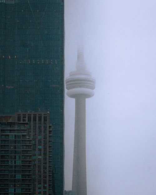Free The CN Tower emerges through fog beside modern skyscrapers, creating a dramatic urban scene. Stock Photo