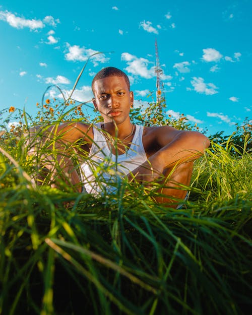 A Man in White Tank  Top Sitting on a Grassy Field