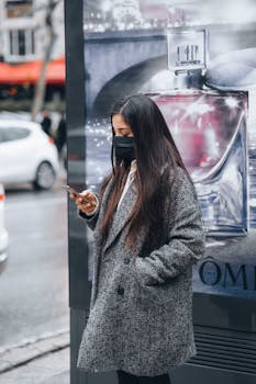 A woman in a coat using her phone on a city street in İstanbul, Türkiye.