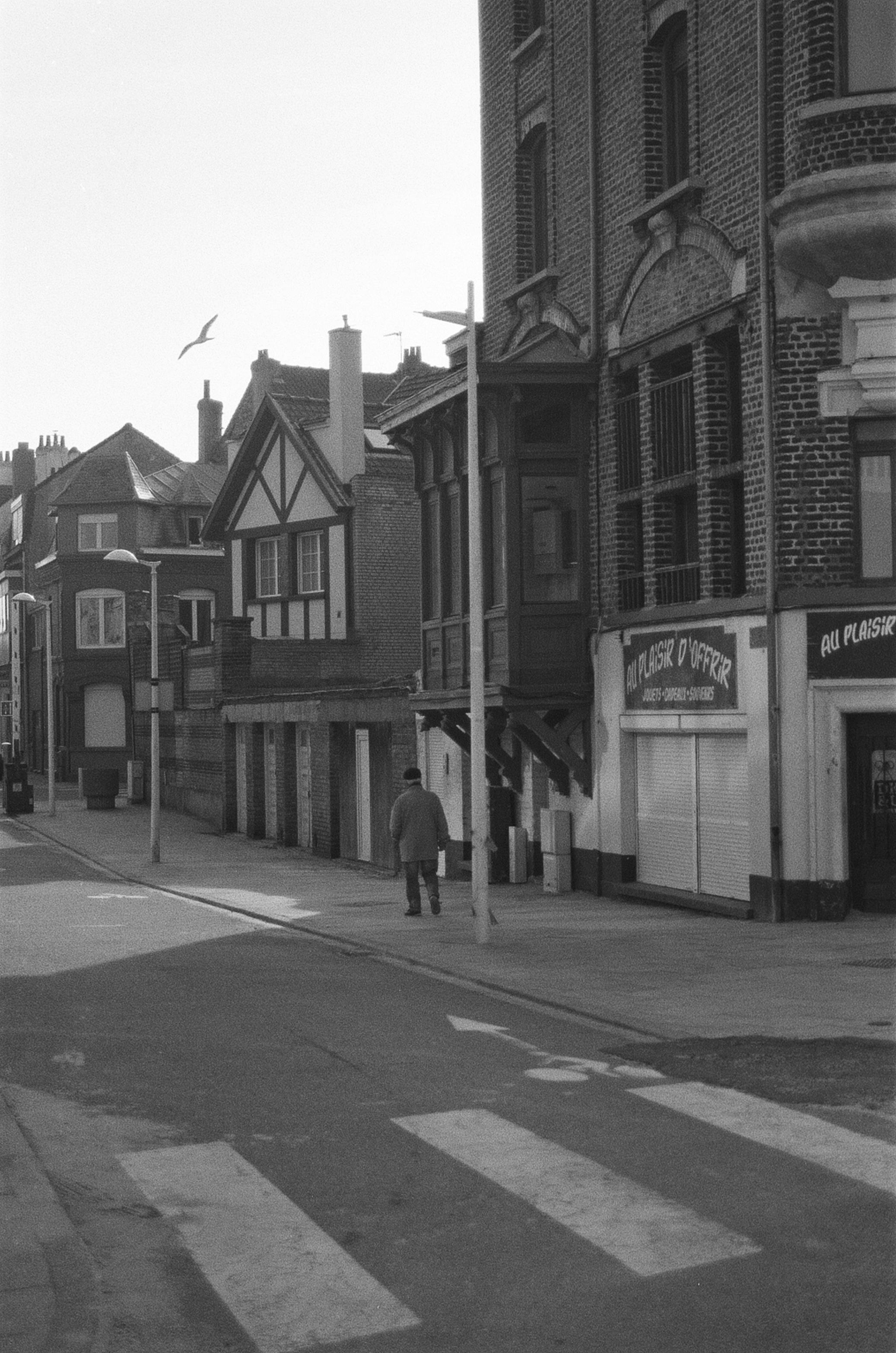 Black and white photo of a person walking along a vintage street with classic architecture.