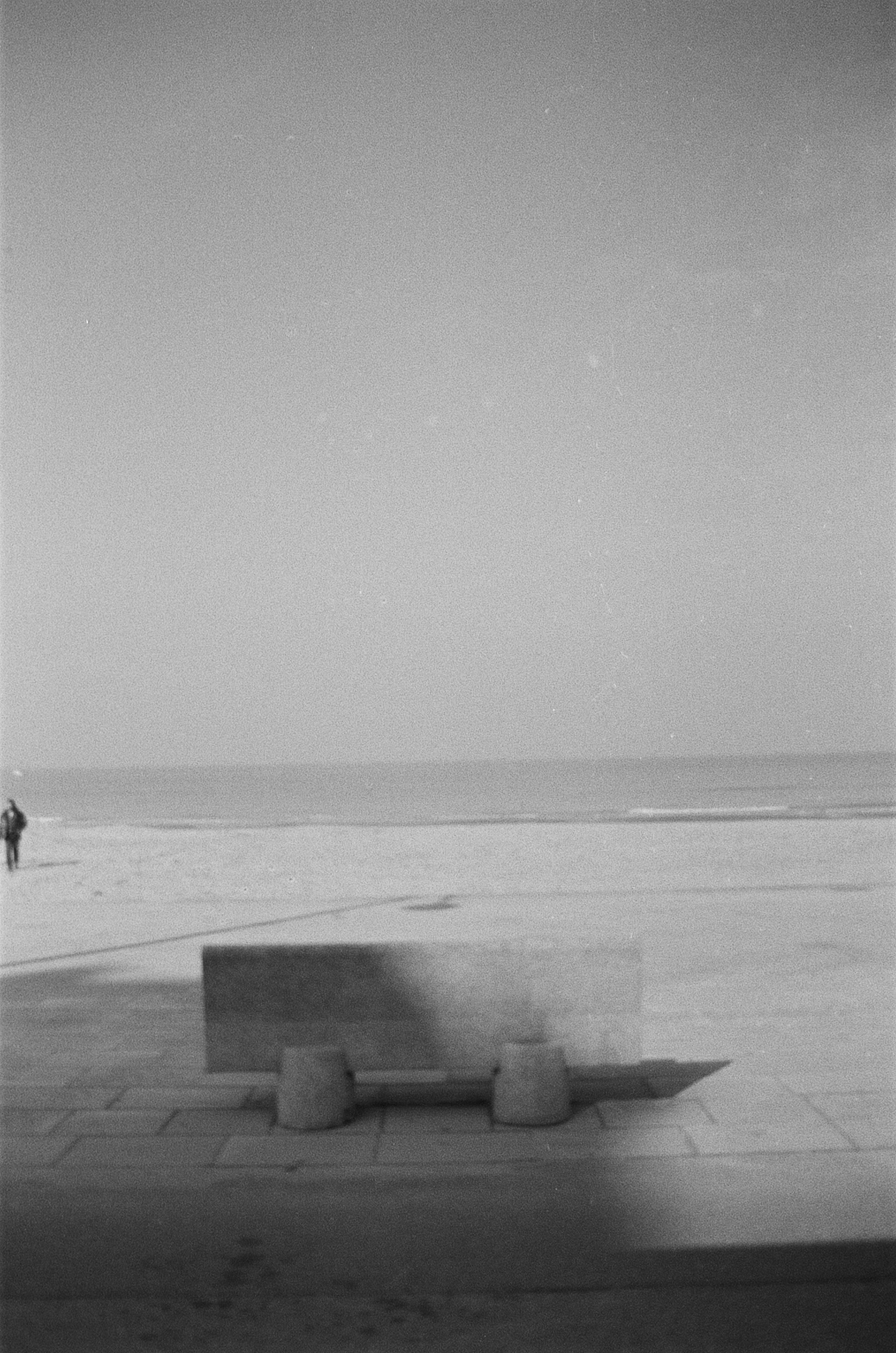 Monochrome image of a concrete bench facing the sea on a deserted beach.