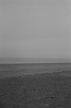 A serene black and white photo of an empty beach with ocean waves in the distance.