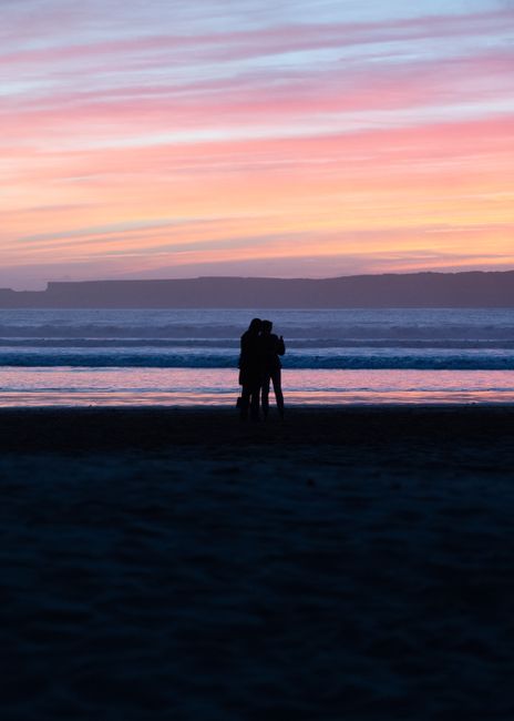 A couple embraces on a Moroccan beach at sunset, capturing the essence of romance.