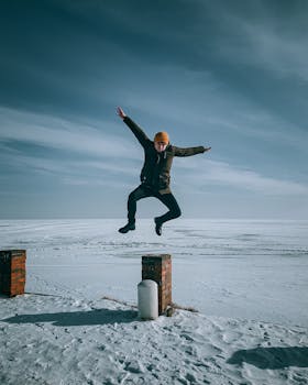 A young man in a jacket leaps midair over a snow-covered landscape, embodying winter fun and adventure.