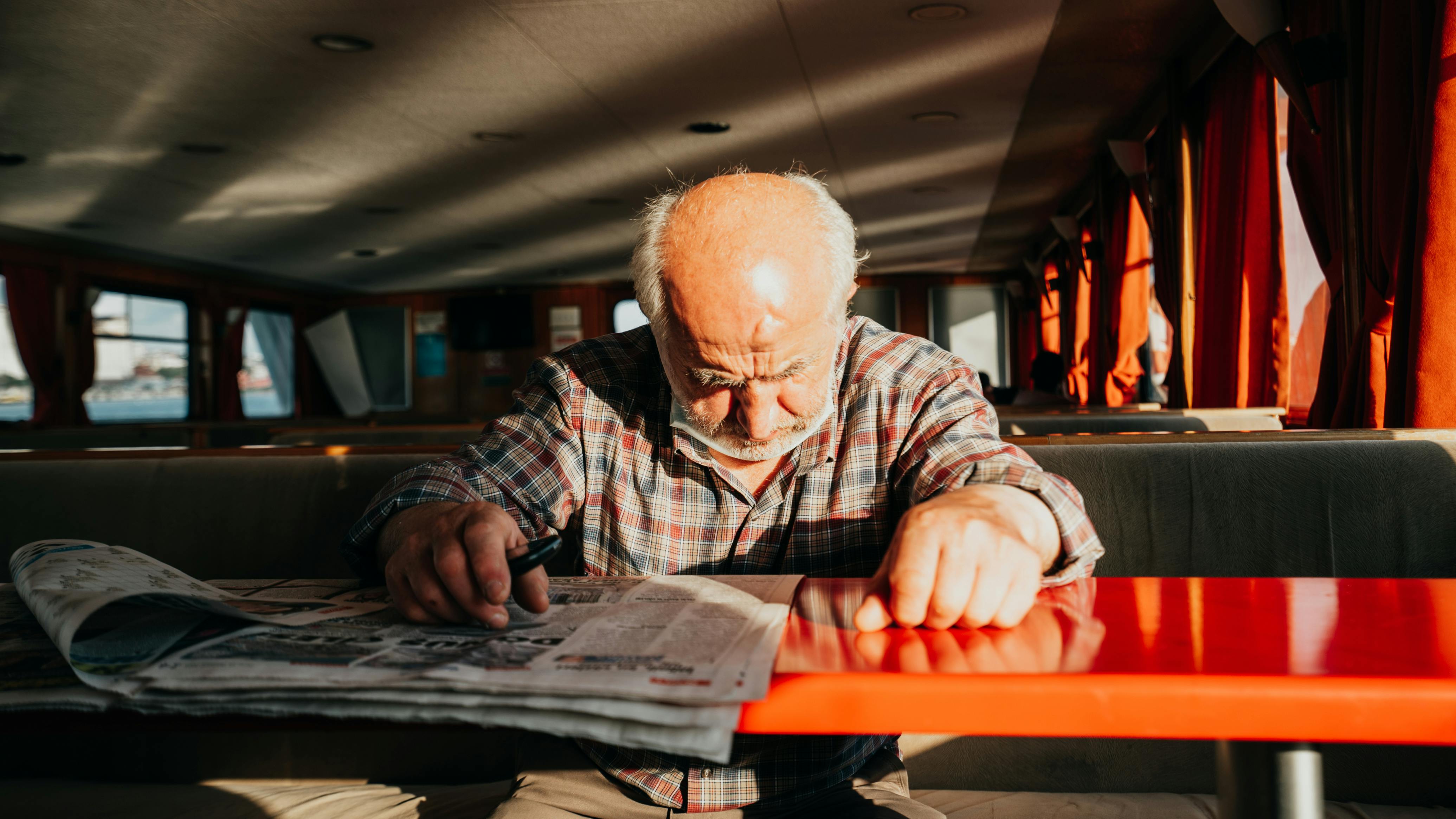Senior man reads a newspaper aboard a ferry in İstanbul, Türkiye, bathed in warm sunlight