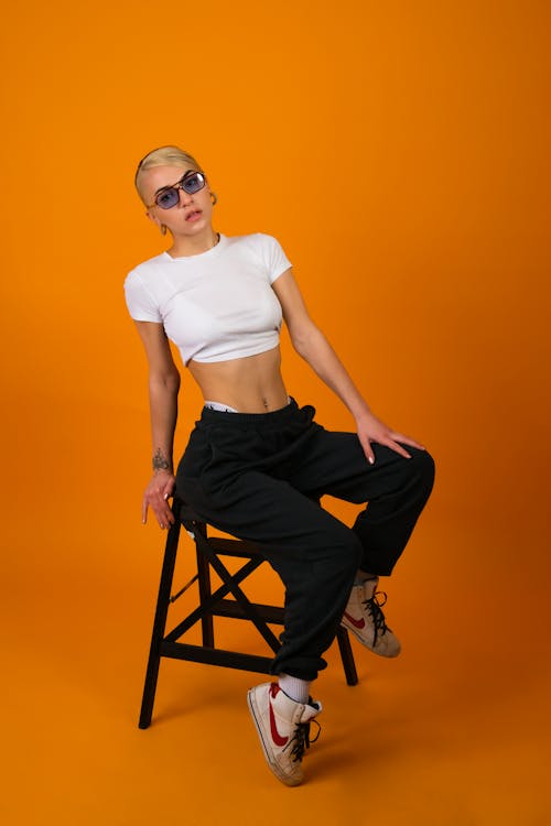 Woman in White Crop Top and Black Jeans Sitting on a Stool