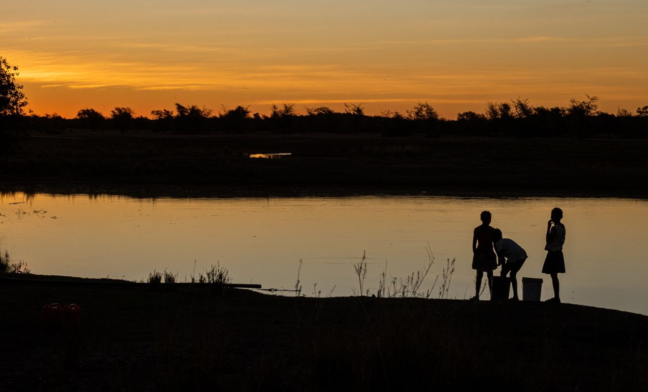 silhouetted children standing by a tranquil lake during a warm dramati