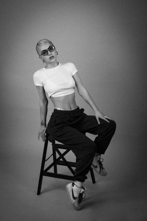 Grayscale Photo of a Woman in White Crop Top Sitting on a Chair