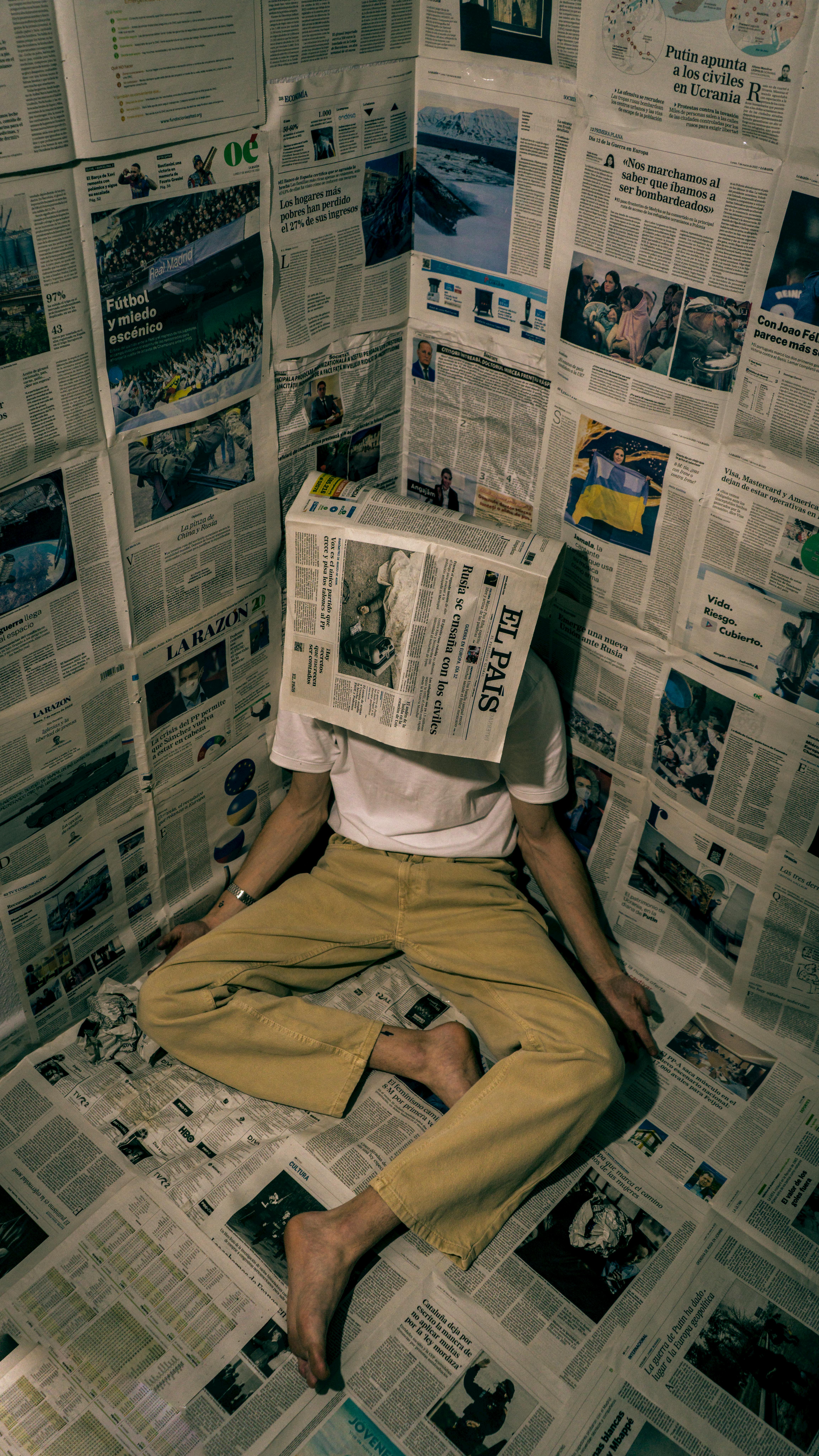 Free Person sitting in a room covered with newspapers, wearing a newspaper hat. Stock Photo