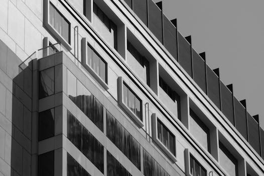 Black and white image of a modern building facade in Hong Kong with reflective glass windows.