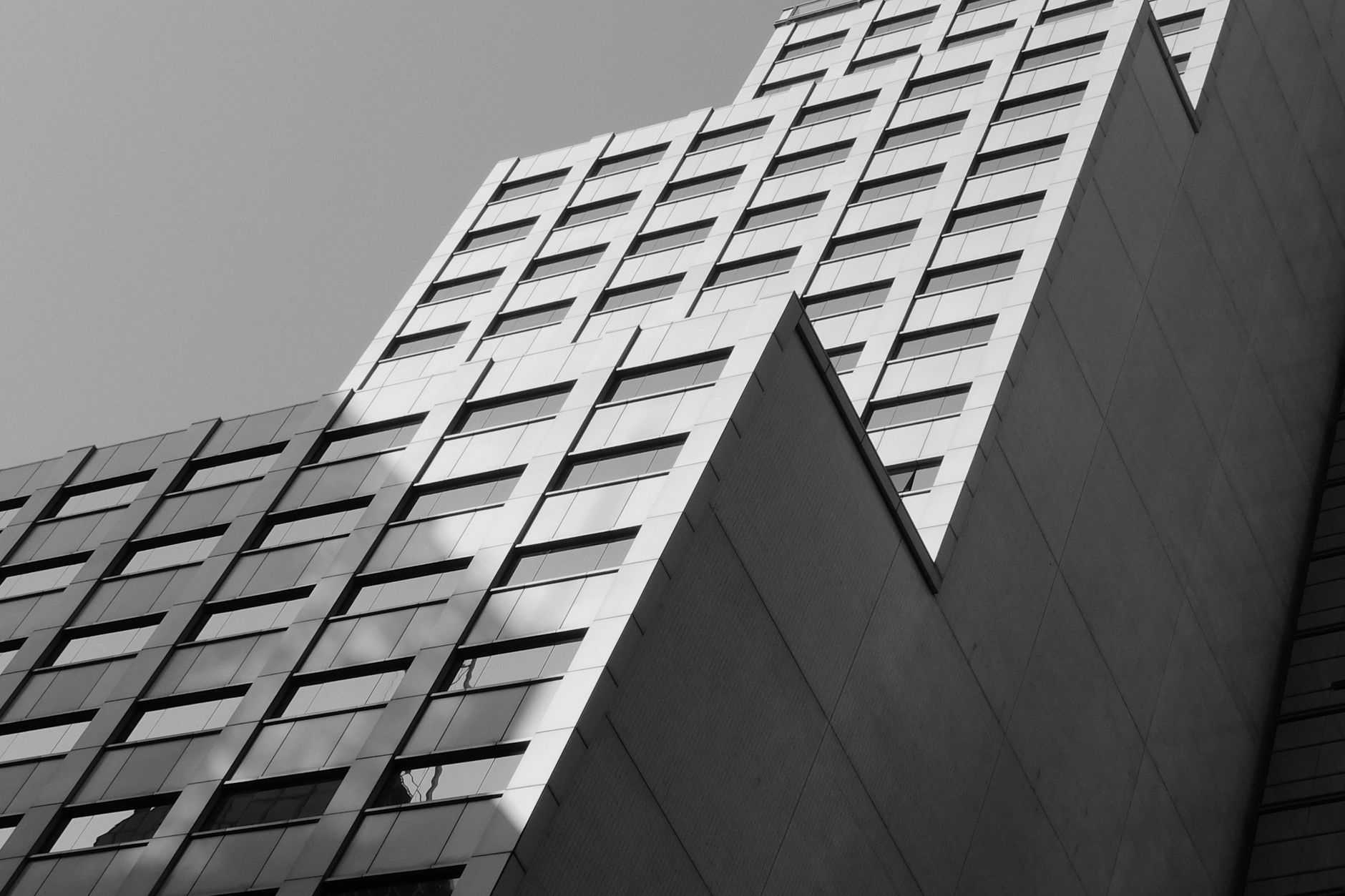 落地窗隱私怎麼做?保留景觀的實用策略 Low angle view of a modern high-rise building with glass windows in Hong Kong, in black and white.