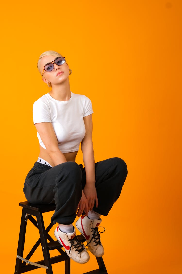 A Woman In White Crop Top And Black Pants Sitting On A Ladder