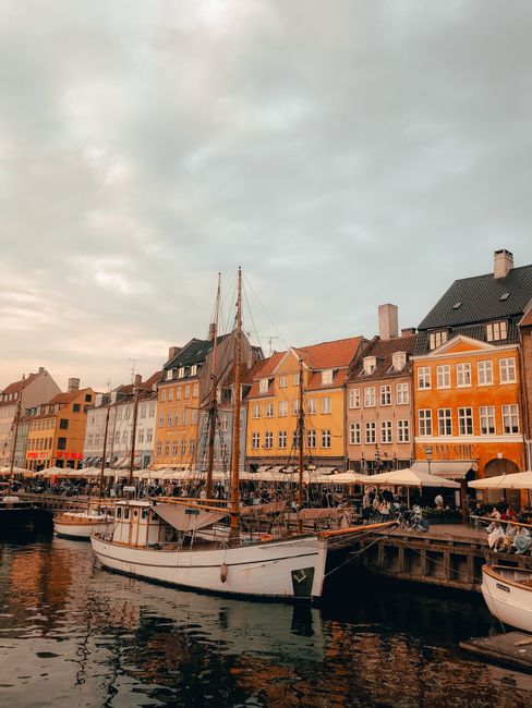 Vibrant facades and sailboats along Copenhagen's Nyhavn canal during sunset.