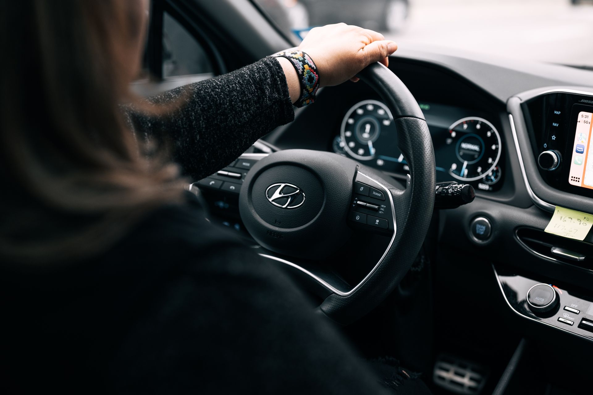 A woman driving a Hyundai car, focusing on the steering wheel and dashboard controls.