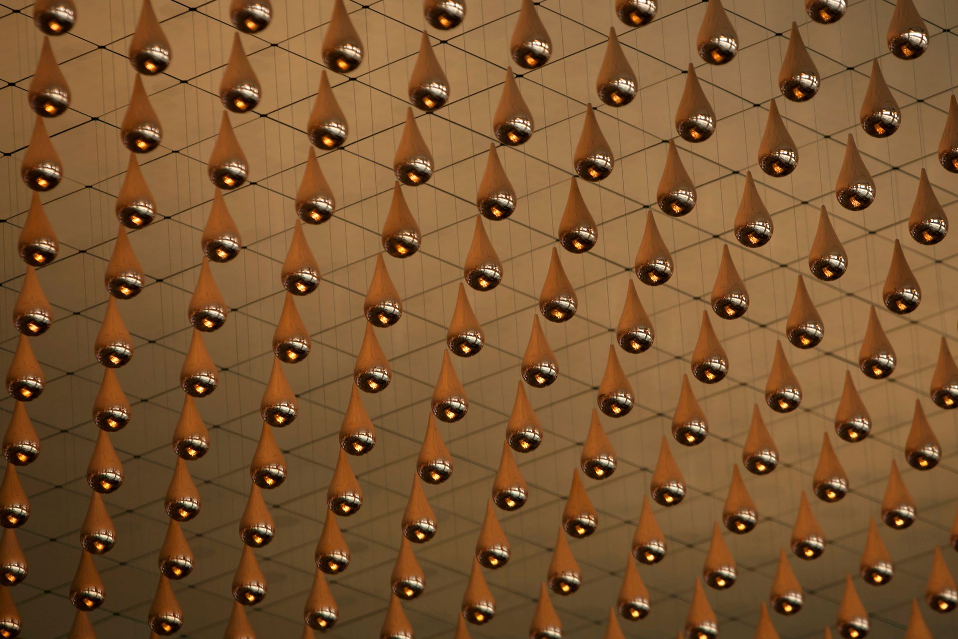 Metallic droplets suspended in an intricate net pattern, creating an immersive art installation.