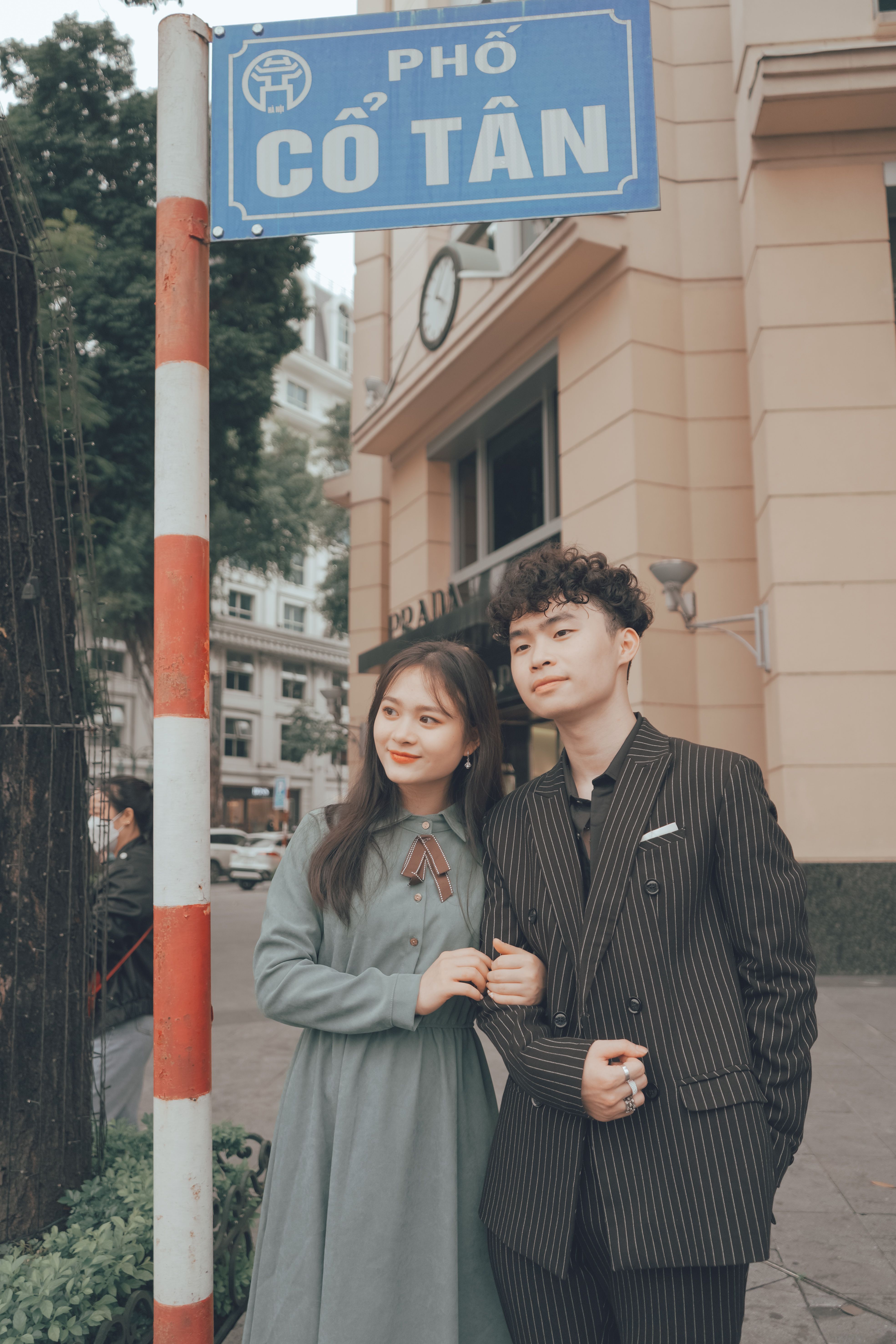 A stylish couple stands smiling on Cổ Tân Street in Hanoi, capturing a moment of urban elegance.
