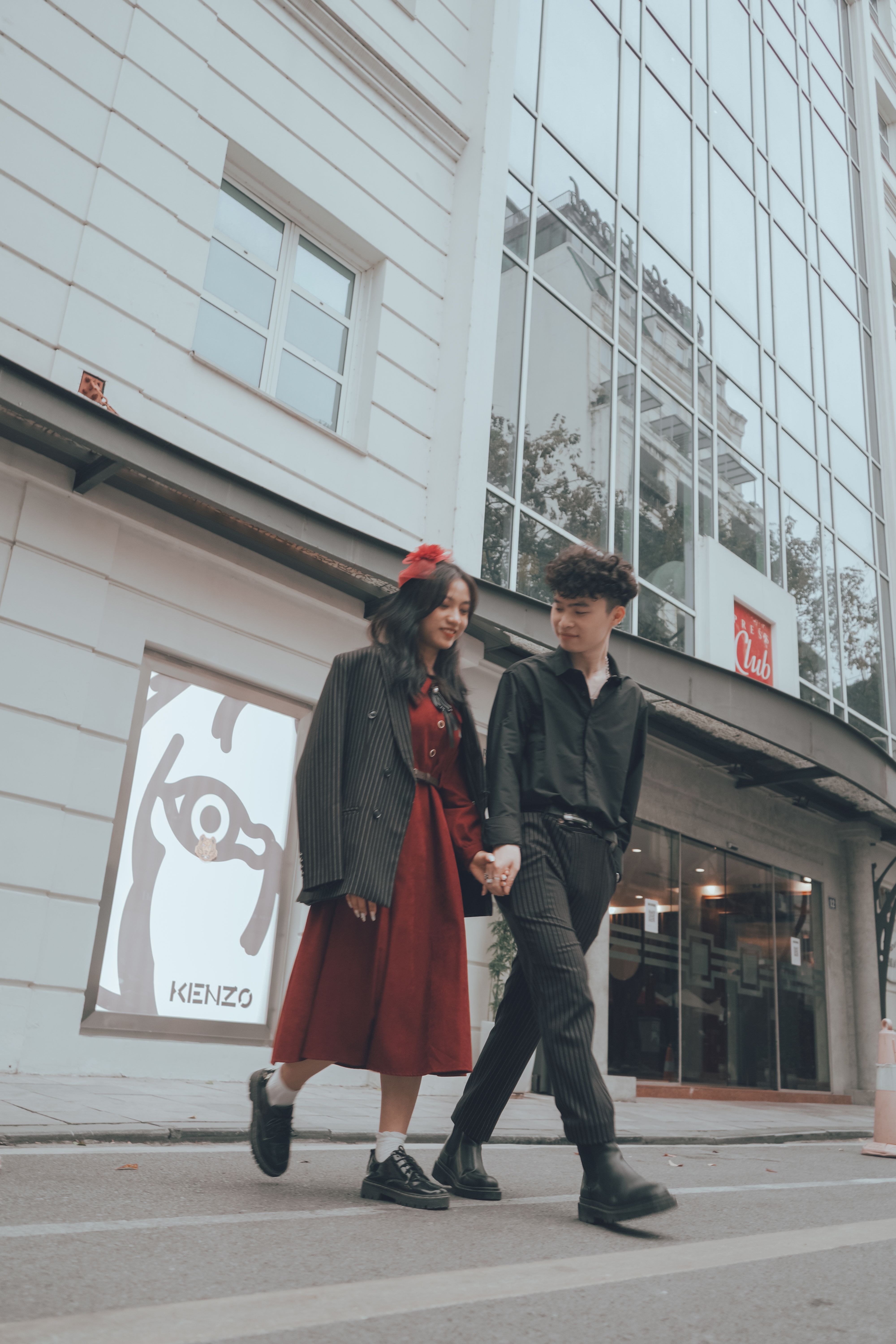 A fashionable couple holding hands while walking outdoors, showcasing modern street style.