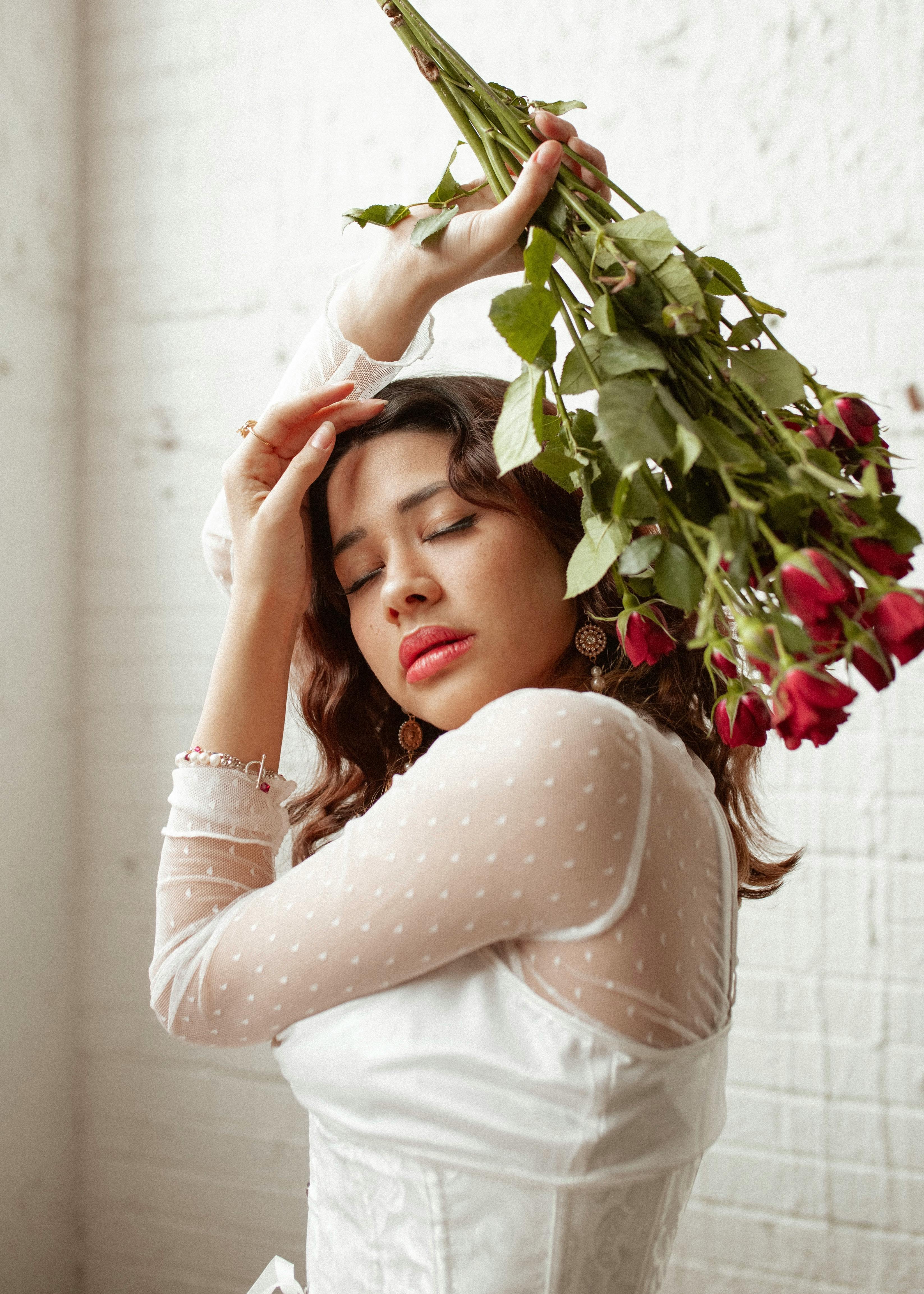 pretty woman in white dress holding bunch of roses above head