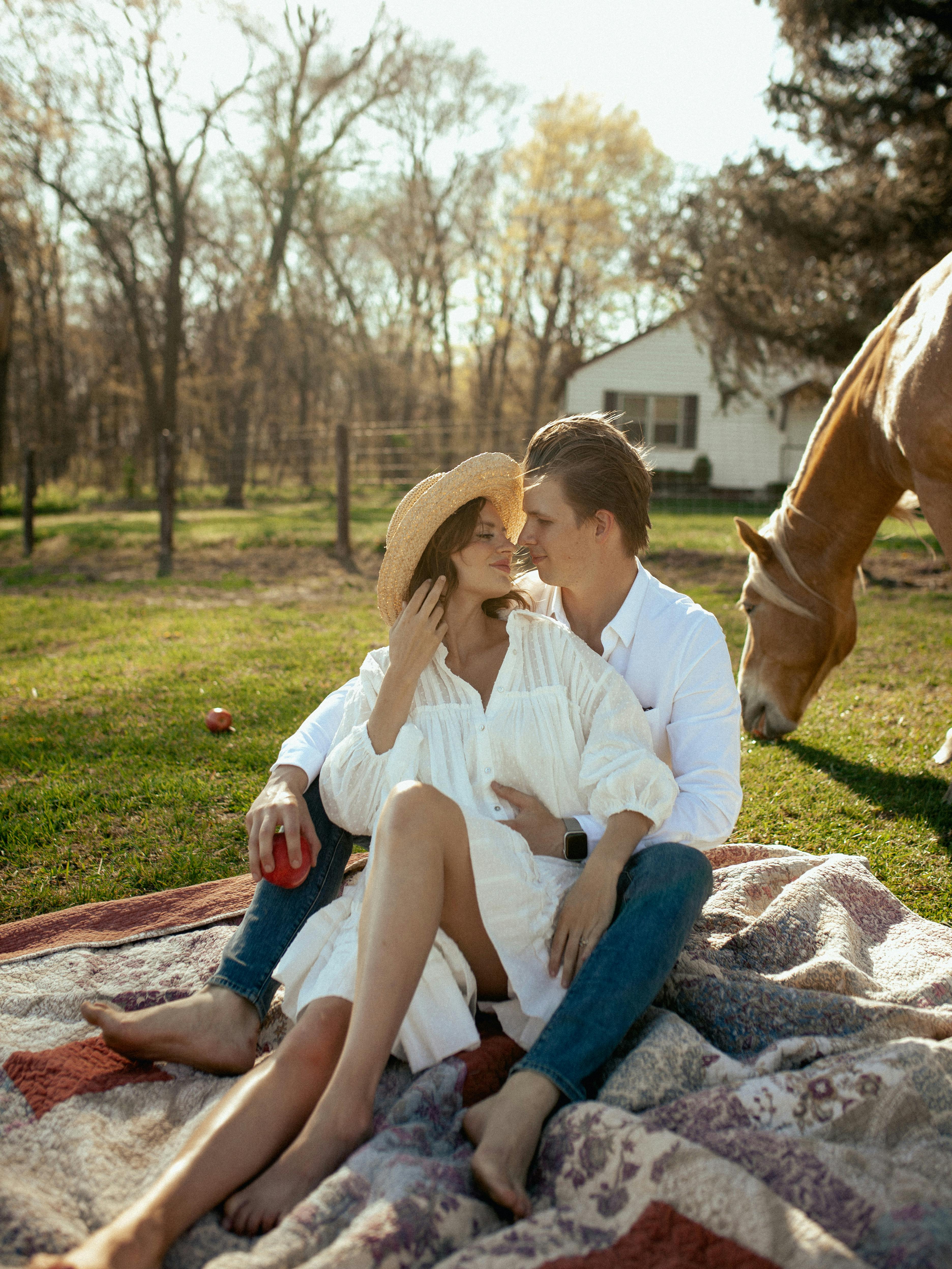 A couple enjoying a cozy picnic outdoors with a horse grazing nearby.