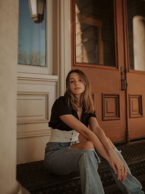 Stylish woman sitting by a wooden door in Des Moines, showcasing casual fashion.