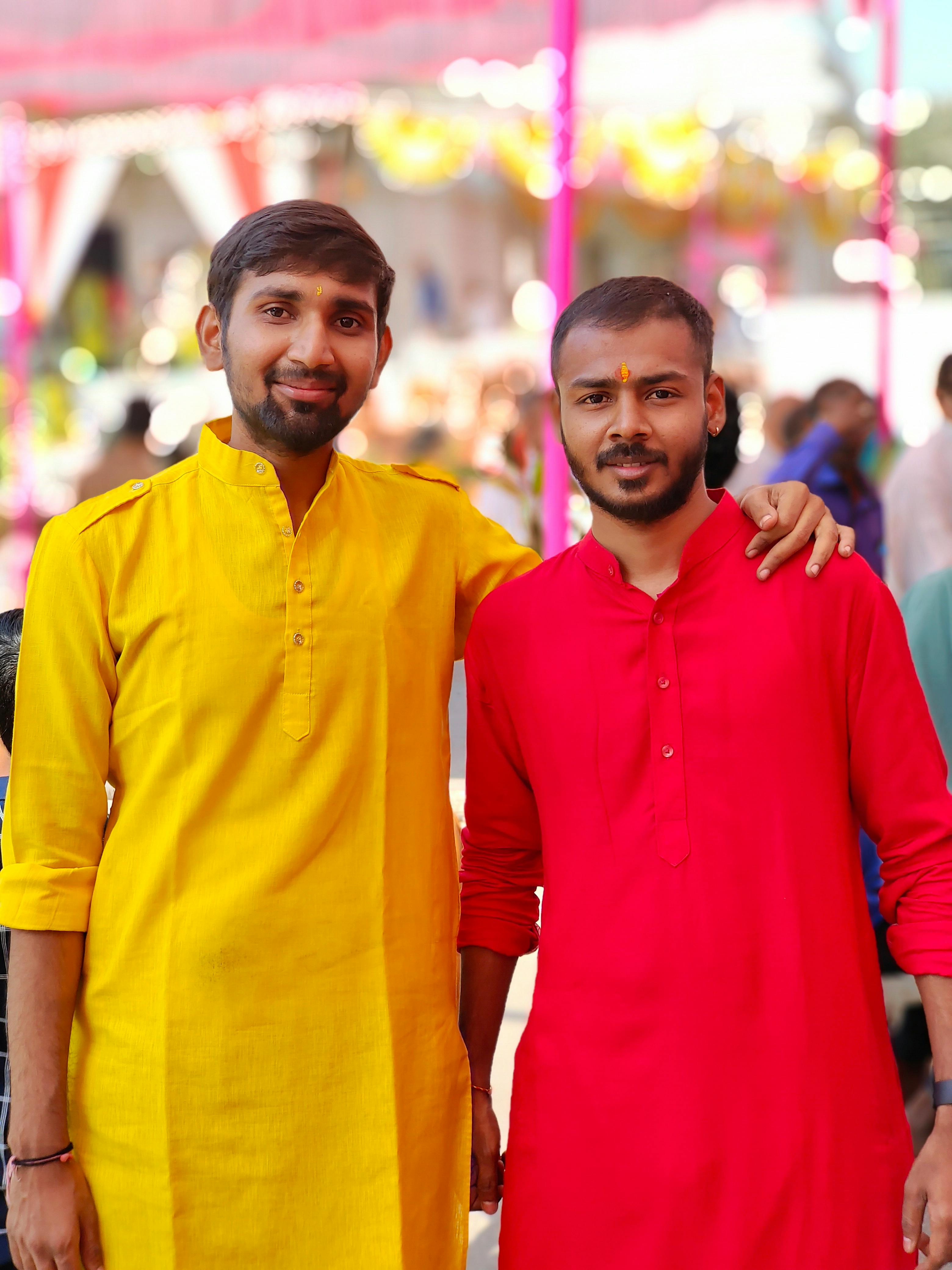 Two smiling men in vibrant traditional attire with a festive blurred background.