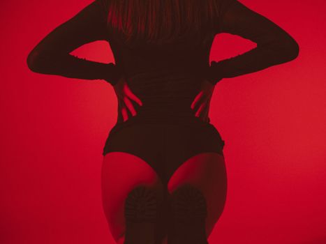 Sensual studio shot of a woman posing in red lighting, showcasing fashion and style.
