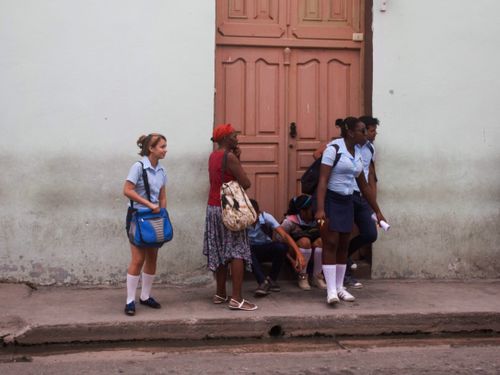 Free A group of students in their school uniforms standing and sitting on a city sidewalk by a wooden door. Stock Photo