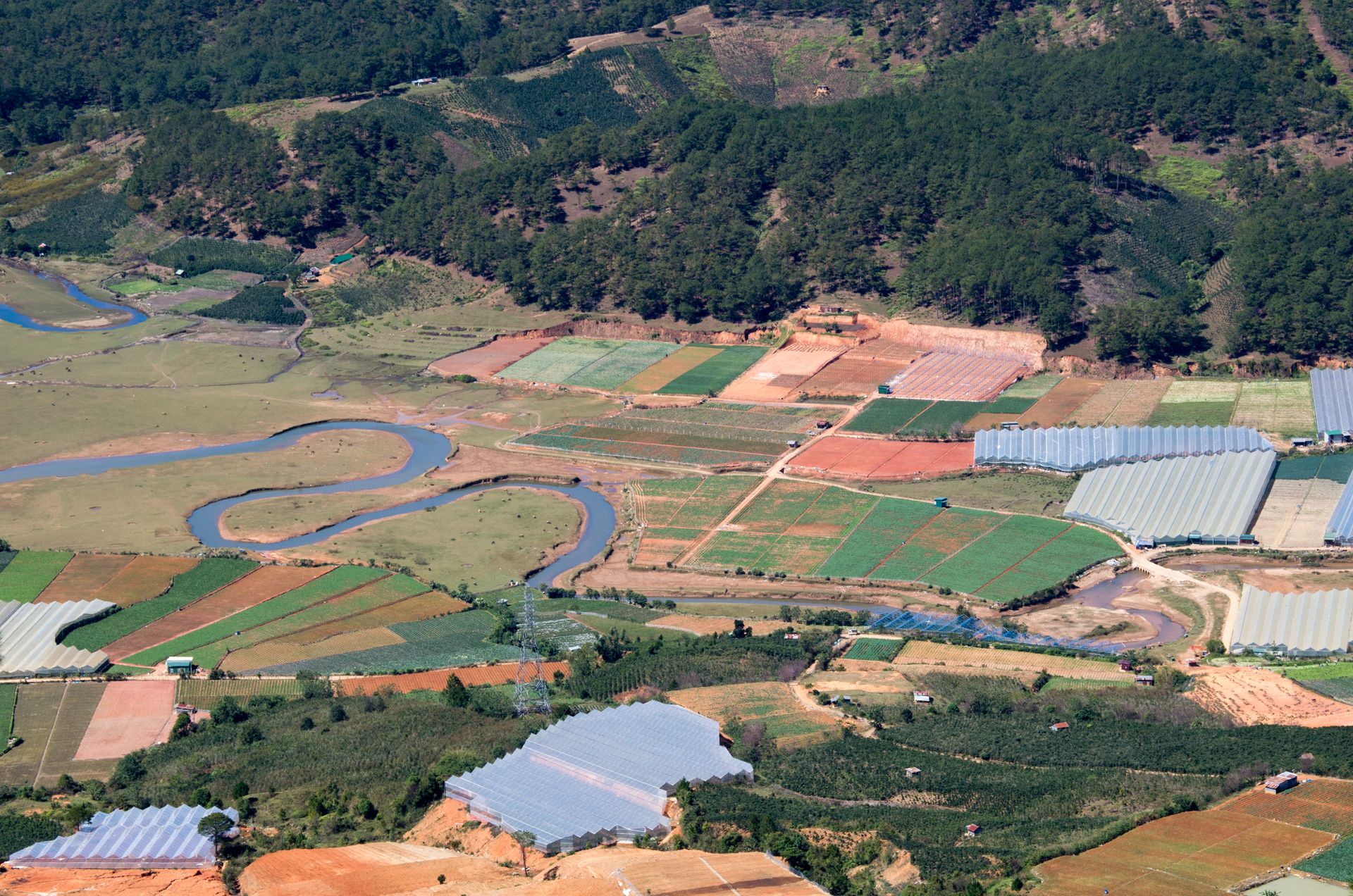 A stunning aerial view showcasing lush agricultural fields and greenhouses in Lâm Đồng, Vietnam.
