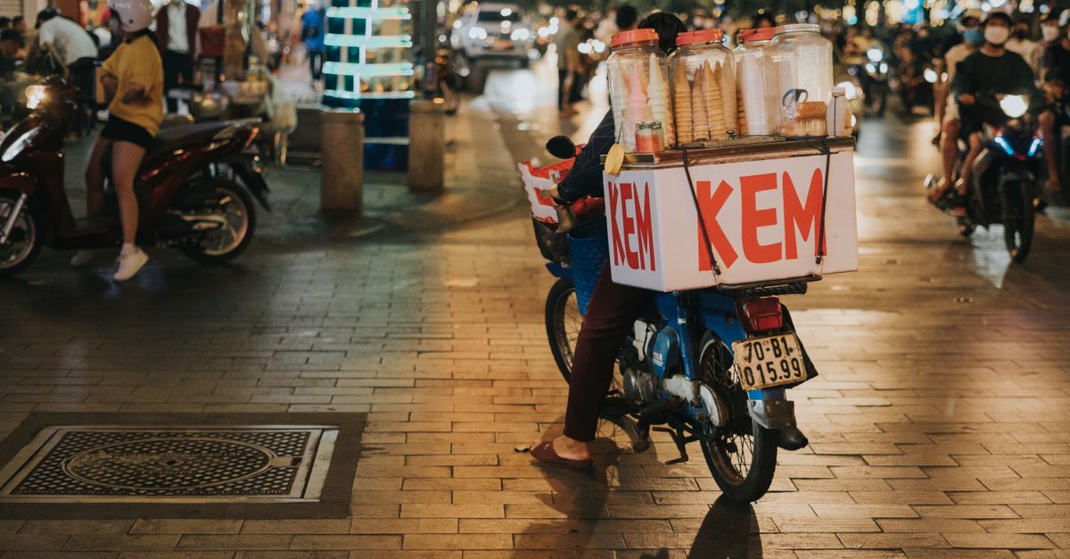 A young Vietnamese entrepreneur serving street food from a modern cart in Ho Chi Minh City, colorful lights