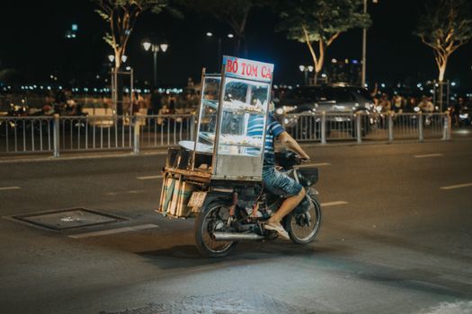 A street food vendor on a motorbike in nighttime Ho Chi Minh City, capturing urban street life.