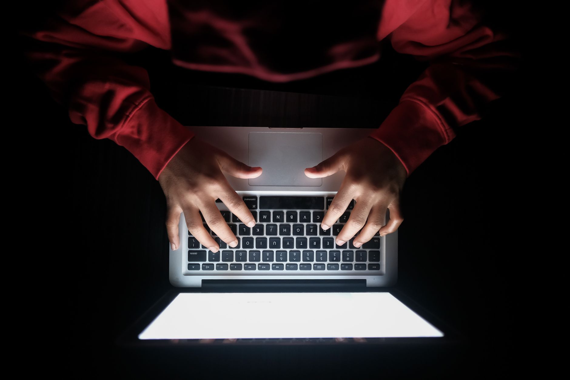 Top view of hands typing on a laptop with a bright screen in a dark setting.