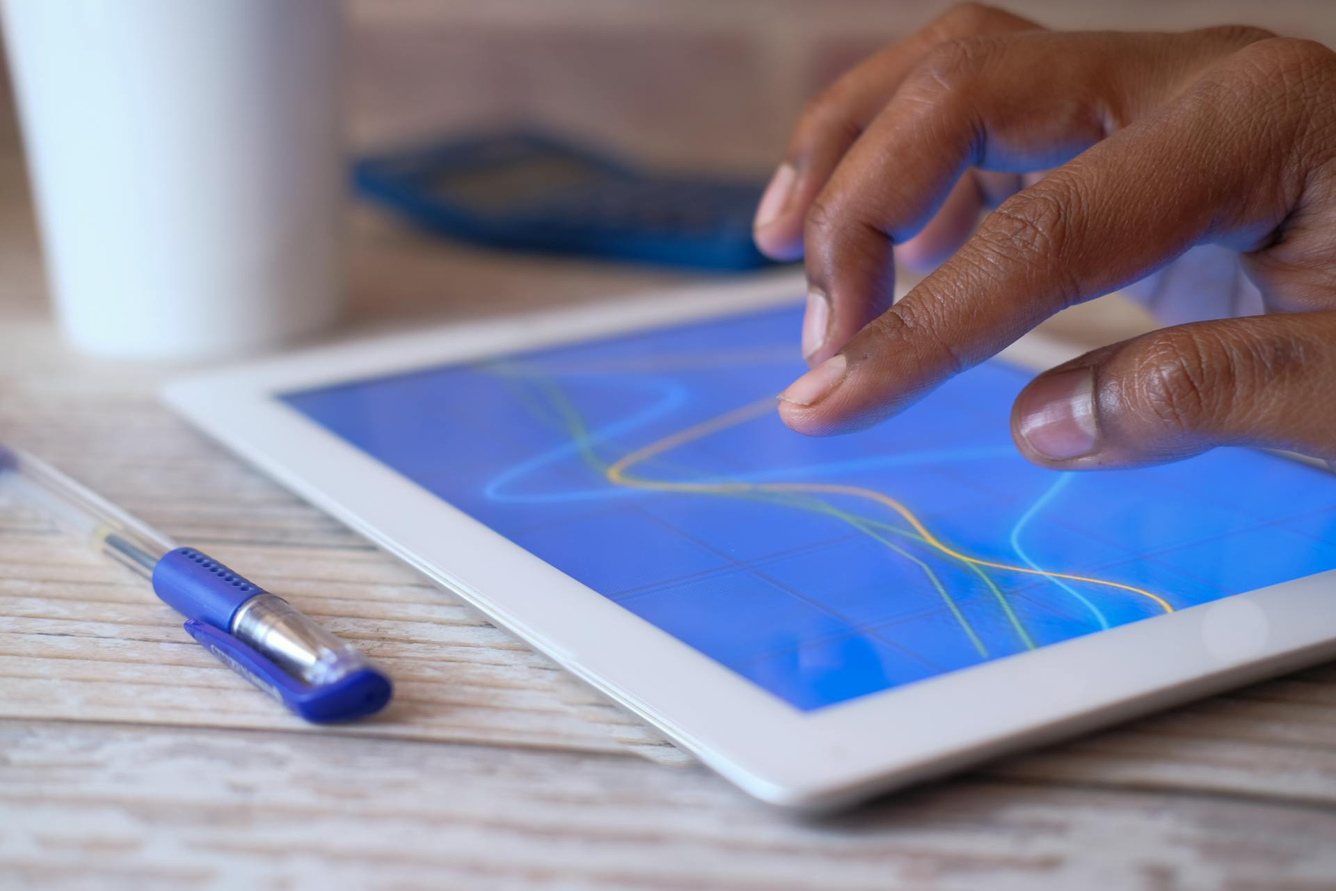 A hand interacting with a digital tablet on a wooden table, showcasing modern technology.